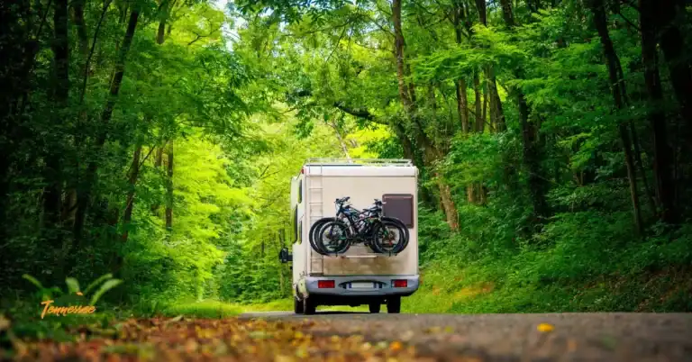 An RV with bikes on the back drives through a mountain road in the Smokies, illustrating a guide to everything you need to know about camping at Cades Cove Campground.