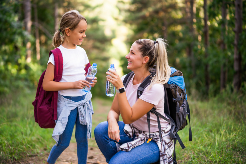 mom and daughter on hiking trail, drinking water, staying hydrated is a essential to hiking.