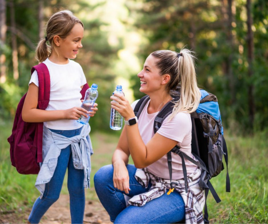 mom and daughter drinking water on hike. staying hydrated