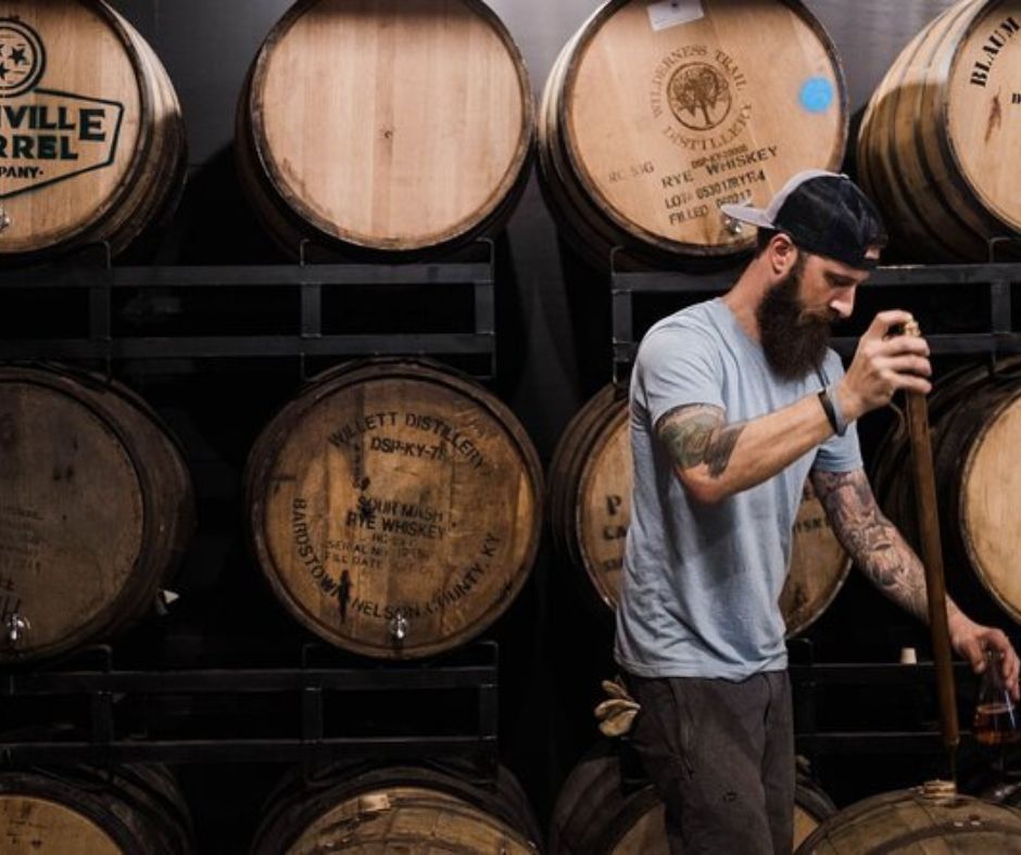 whiskey barrels with a man removing whiskey with special tool.