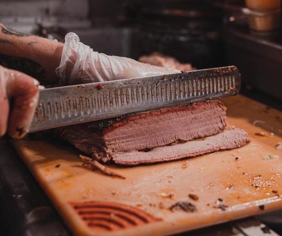 large knife slicing slab of smoked meat, bbq, on a wooden surface