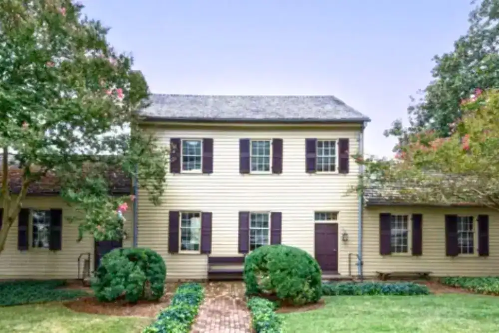 Blount Mansion, a two-story cream-colored 18th-century home in Knoxville with dark shutters, a brick walkway, and lush boxwood gardens