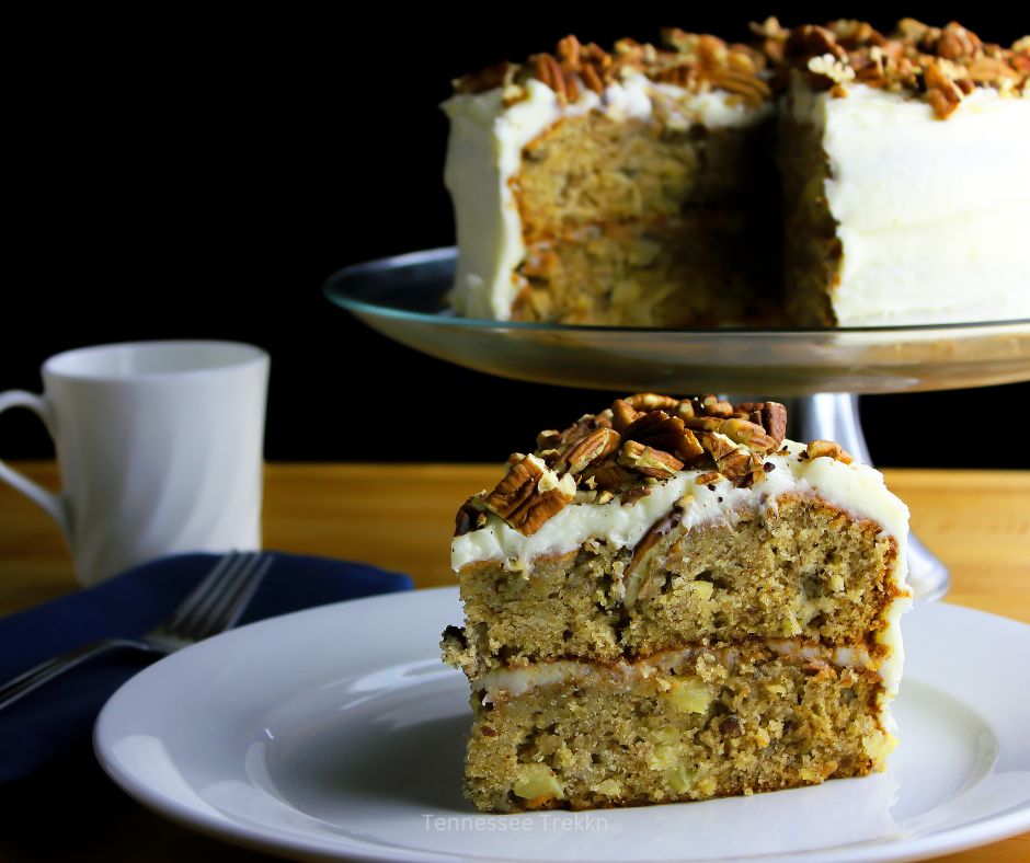 A slice of hummingbird cake on a plate next to a cup of coffee.