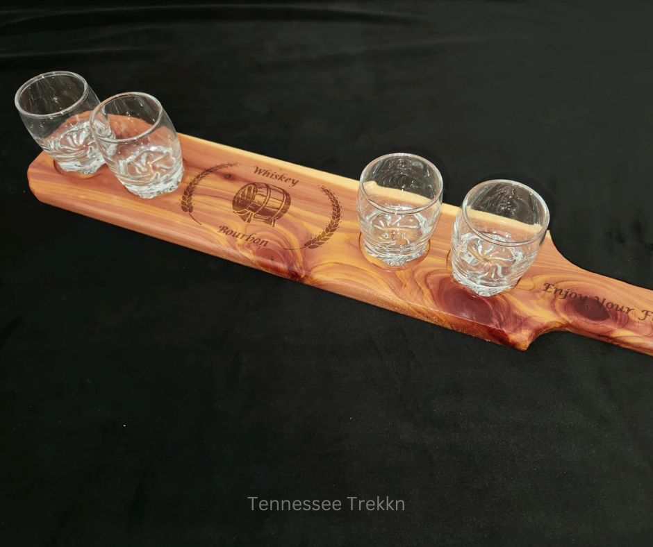 A handcrafted bourbon flight board by Mark’s Beautiful Creations, featuring four glasses and a stylish wooden design.