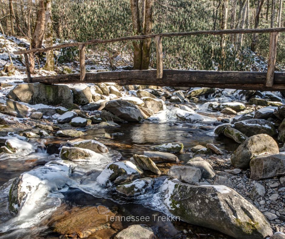 A scenic walkover bridge crossing a creek with snow-dusted surroundings on a winter hiking trail.