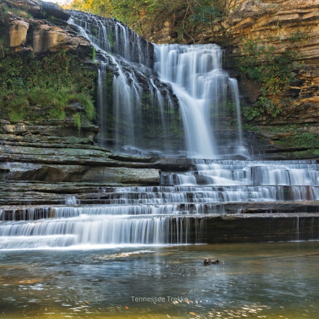 A picturesque view of Cummins Falls, a cascading waterfall in Tennessee, surrounded by rocky cliffs and lush greenery.