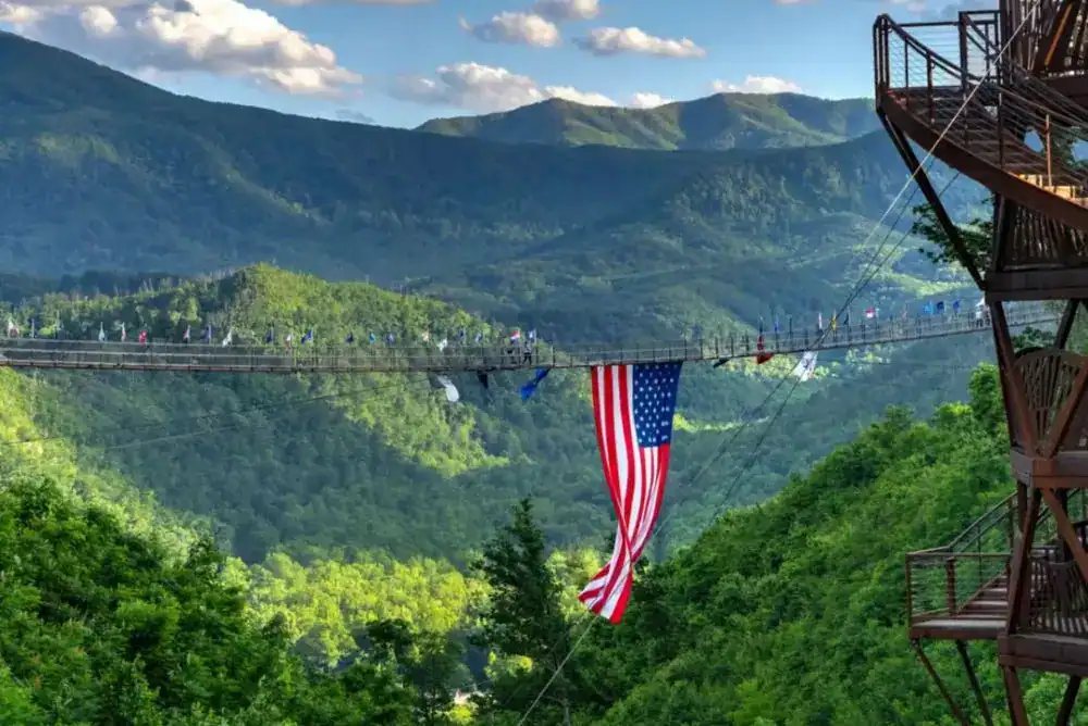 SkyBridge stretching across a green Smoky Mountain valley with an American flag at its center and the Tulip Tower to the side
