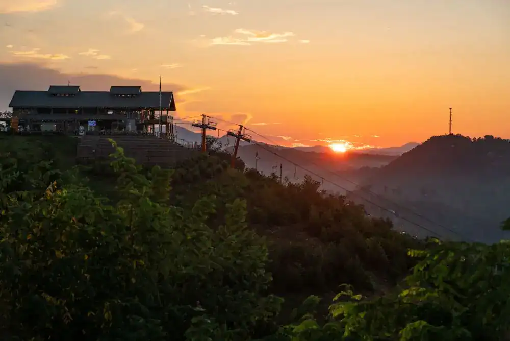 Sunset over the Smoky Mountains from Gatlinburg SkyPark, with the SkyCenter building on the ridge and the sun dropping behind the hills