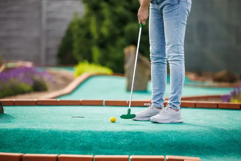 A person in jeans putting a yellow golf ball on a green mini golf course in Pigeon Forge
