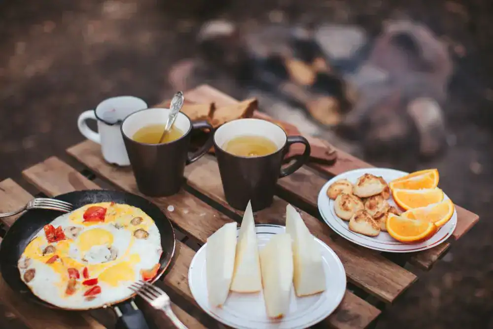 Delicious campfire breakfast – eggs in a cast iron skillet paired with warm tea, perfect for outdoor mornings.