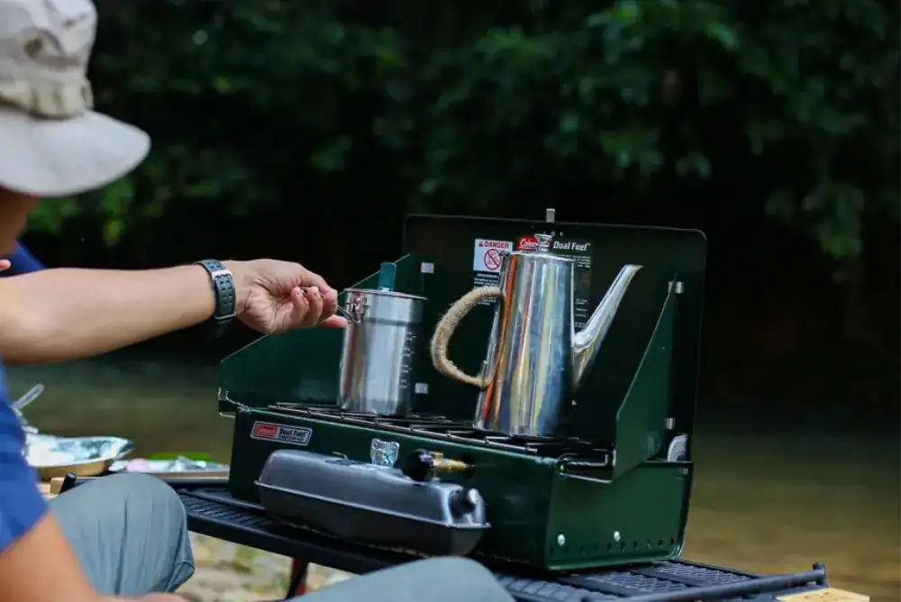 Kettle heating on a stove at a campsite, perfect for making coffee or tea.