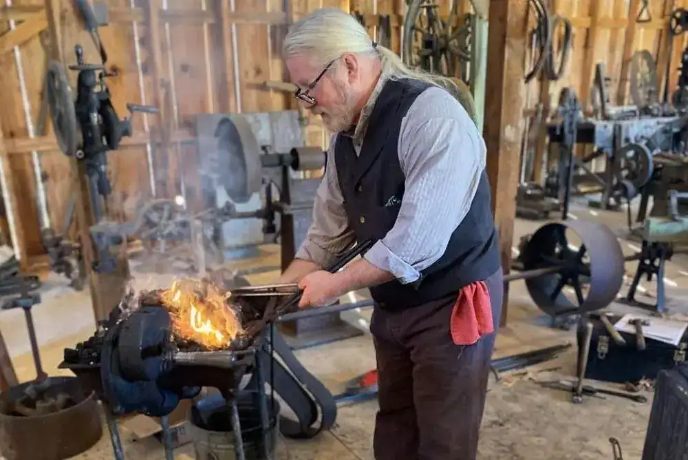Blacksmith working at a forge inside a historic workshop at the Great Smoky Mountains Heritage Center in Townsend, Tennessee.