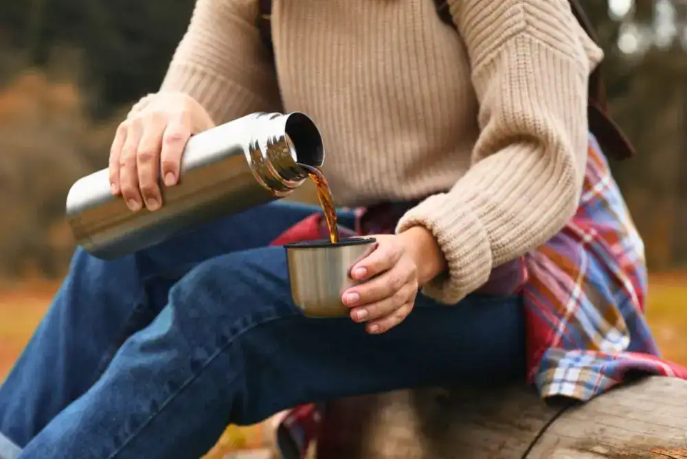Pouring hot coffee from a thermos, a must-pack item for a chilly morning in the fall.