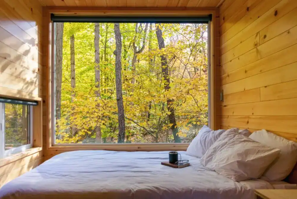 Cozy bed inside a Smoky Mountain treehouse with large windows and mountain views, perfect for a peaceful glamping getaway.