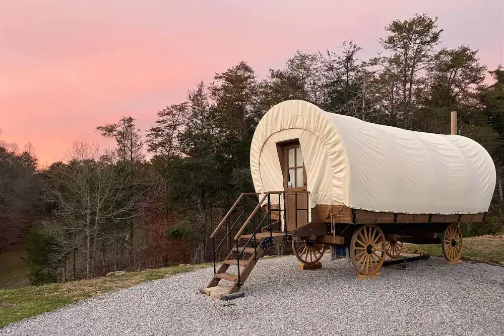 Rustic covered wagon glamping setup at Smoky Hollow Outdoor Resort with mountain views and cozy outdoor seating.