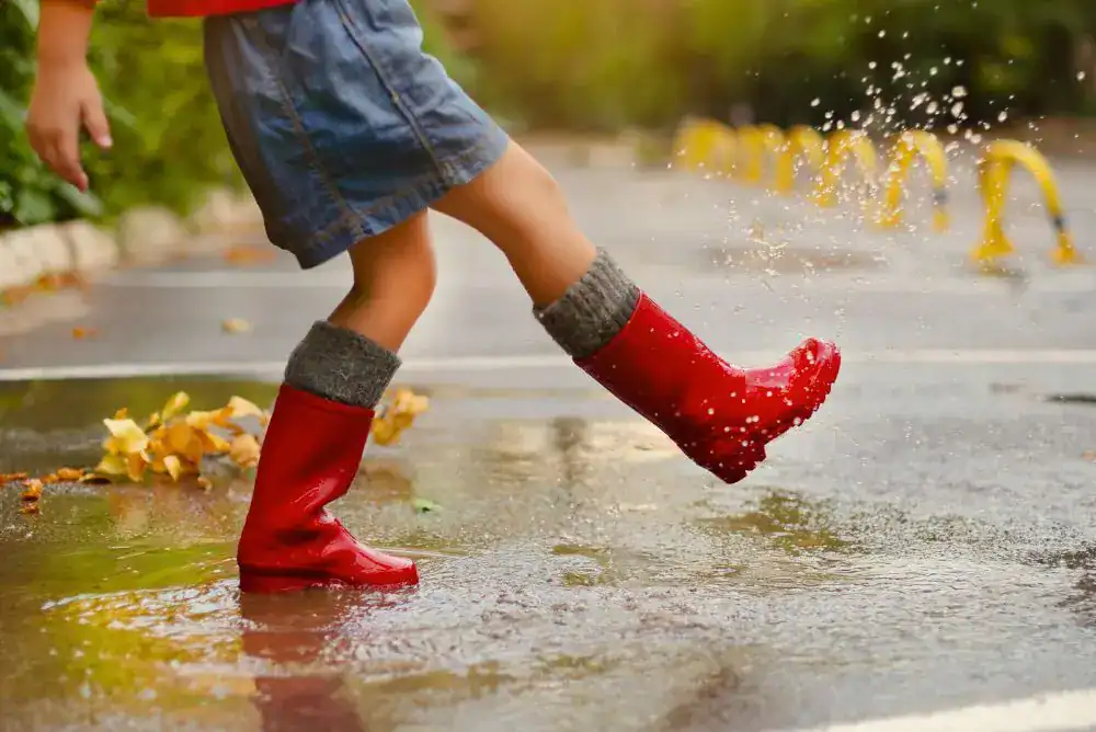 Kid playing outside in the rain with red rain boots, featured in our kids gift guide.