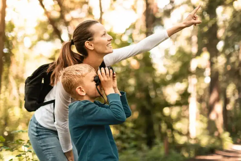 Mom and son outdoors with the child looking through binoculars during a nature adventure.