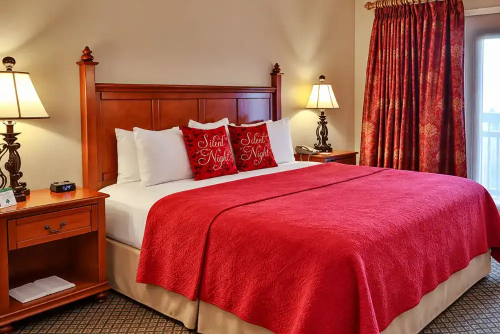 King guest room at The Inn at Christmas Place in Pigeon Forge, featuring red bedding, Christmas pillows, and wooden furniture.