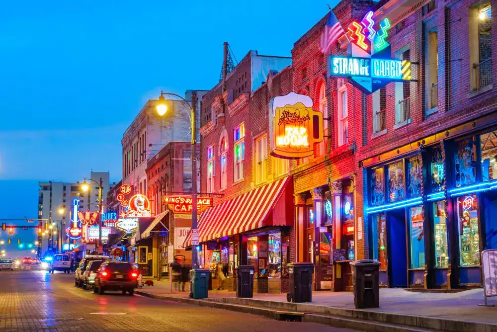 A neon-lit street of music clubs and restaurants on Beale Street in downtown Memphis at dusk, perfect for a Tennessee city weekend getaway. 