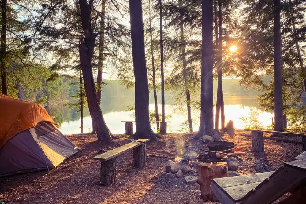 Tent campsite beside a lake at sunrise in an East Tennessee state park, with a campfire area and nearby hiking trails.