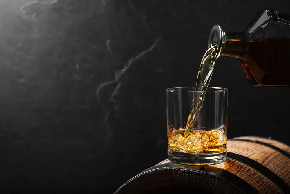 Whiskey being poured into a glass resting on a barrel, representing the Tennessee Whiskey Trail distillery experience