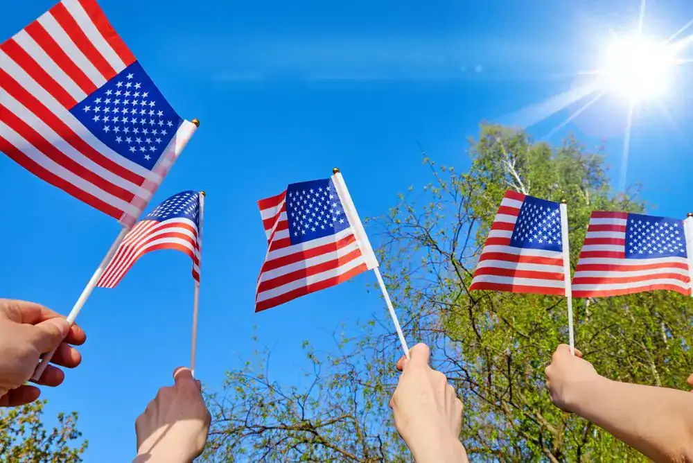 Family members holding American flags together while celebrating the Fourth of July outdoors on a sunny summer day. Perfect for enjoying our July 4th kid drinks