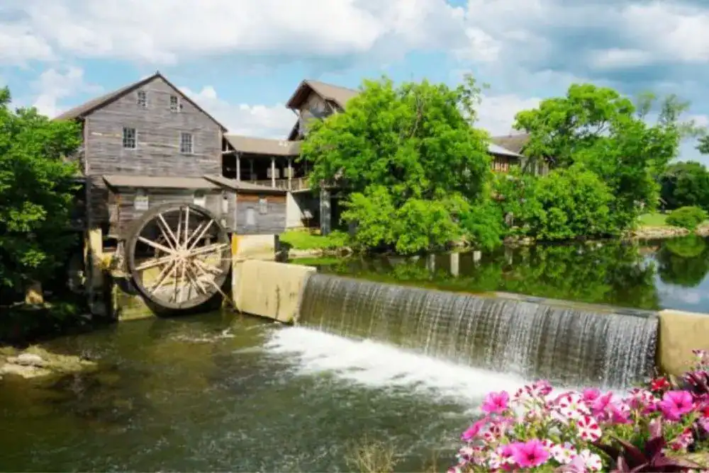 The Old Mill in Pigeon Forge, Tennessee, with its historic waterwheel, flowing river, and colorful flowers in the foreground.