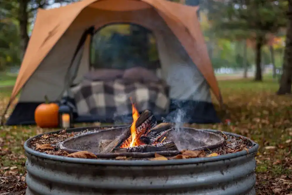 Fall camping essentials at a cozy campsite with a tent, warm blanket, and campfire.