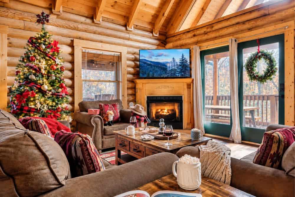 Christmas-decorated log cabin living room in Gatlinburg with a Christmas tree, fireplace, and rustic wood interior.