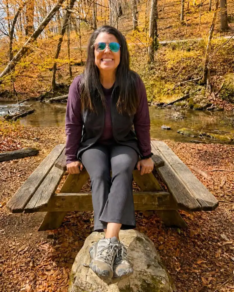 Angela sitting on a picnic table by a creek in the fall