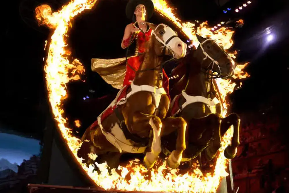 Two horses and their riders performing a trick through a ring of fire at Dolly Parton's Stampede in Pigeon Forge.