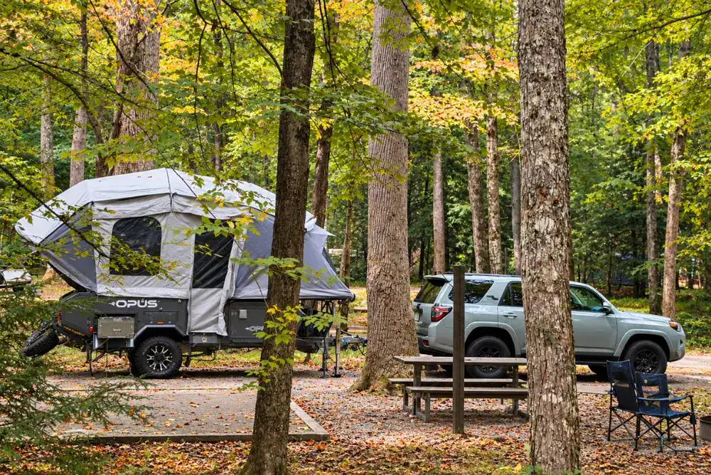 Pop-up camper and SUV at a wooded Smoky Mountains campsite with a picnic table and camping chairs.